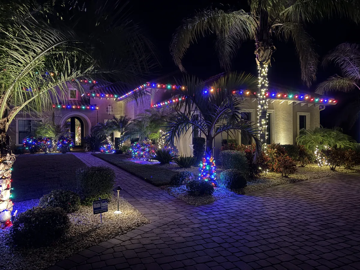Residential Christmas light installation with a multicolor roofline and light-wrapped palms