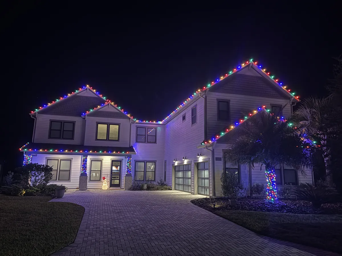 Two-story home with a multicolor Christmas light roofline installed by Green Life